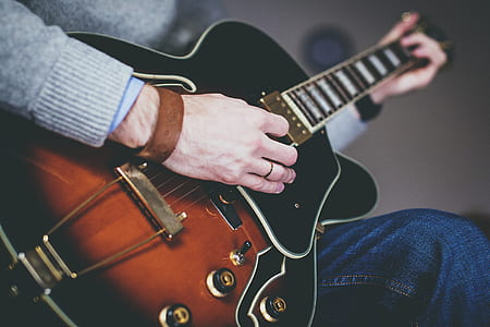 person in gray sweater and blue denim bottoms playing guitar thumbnail