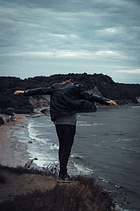 Man Standing On Cliff Facing Body Of Water thumbnail