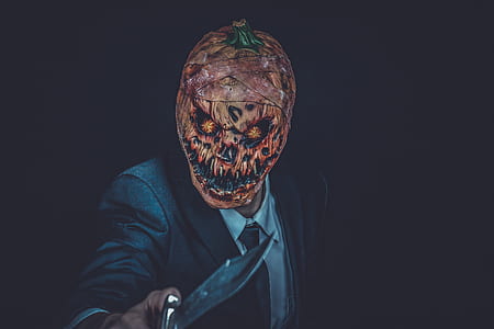 person in black coat holding silver knife wearing orange scary mask thumbnail
