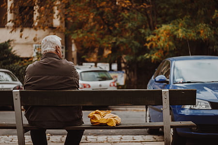 man wearing brown jacket sitting on bench looking at car thumbnail