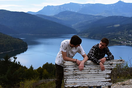 Two Person Standing at the Back of White Wooden Board Near the Body of Water thumbnail