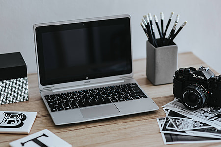 Black-and-white photos with a silver laptop, a smartphone, car keys, pencils and a camera thumbnail