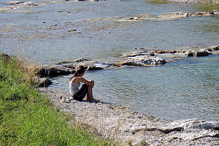 woman sitting on ground facing body of water thumbnail