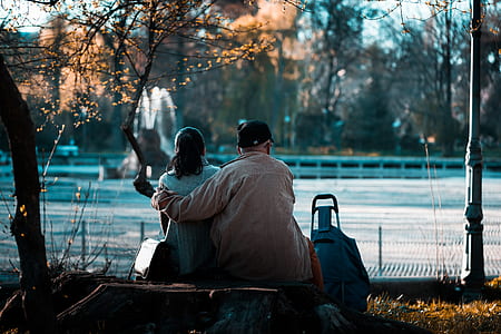 man hugging woman while sitting on street bench thumbnail
