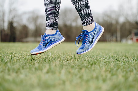 person wearing blue Nike running shoes jumping on hair above green grass field thumbnail