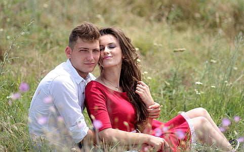 woman and man near each other while sitting on grass field during daytime thumbnail