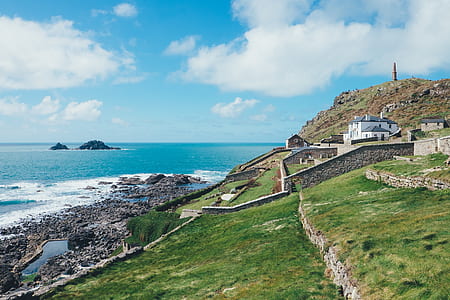 green grass field near sea under blue sky thumbnail