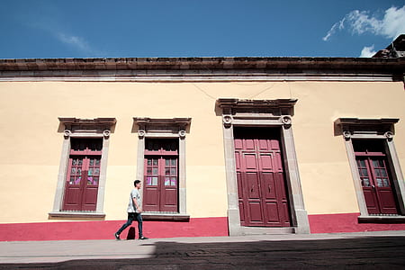 person walking beside yellow and red concrete building thumbnail