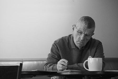 grayscale photography of man sitting while holding pen on table thumbnail