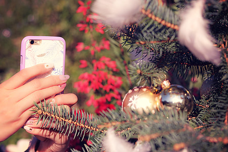 selective photography of person holding phone taking photo on christmas tree thumbnail
