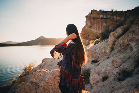 woman standing on mountain cliff across body of water thumbnail