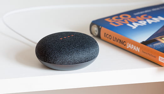 charcoal Google Home mini speaker beside orange book thumbnail