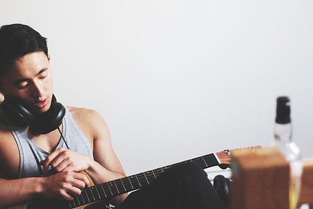 man wearing gray tank top holding guitar inside well-lit room thumbnail