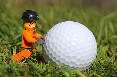 orange minifig pushing golf ball on green grass thumbnail