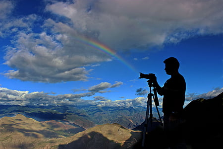 silhouette of man standing beside camera placed on tripod thumbnail