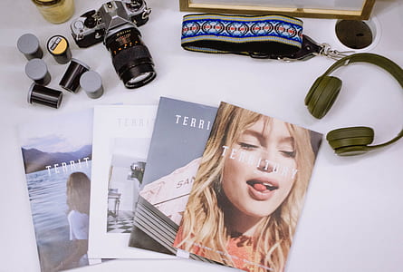 gray and black DSLR camera near gray cordless headphones and four assorted magazines thumbnail
