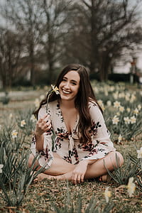 woman holding daffodil flower sitting on daffodil field during daytime thumbnail