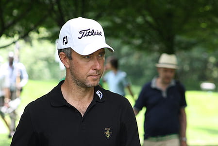 man wearing white Titleist cap walking under green tree during day thumbnail