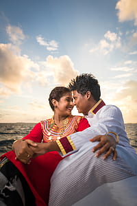man and woman sitting and facing each other while holding hands under white clouds and blue sky thumbnail