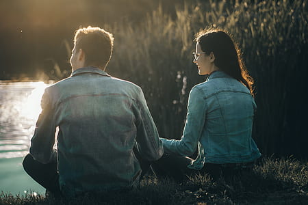 man and woman sitting on field near body of water thumbnail