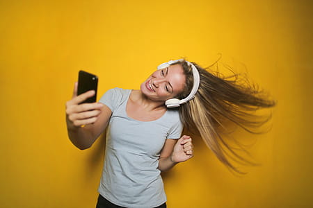 Young woman dancing and listening to music with wireless headphones connected to smart phone, isolated on yellow background thumbnail