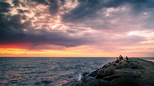 group of three people sitting on rock formation near body of water thumbnail