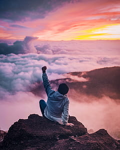 person sitting on cliff raising his left hand thumbnail