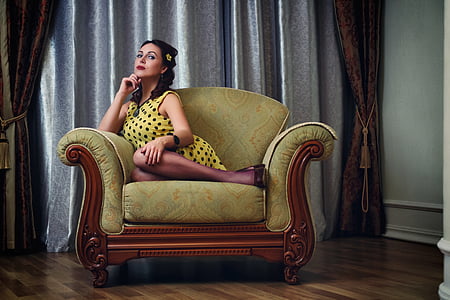 woman sits on green padded brown wooden sofa chair thumbnail