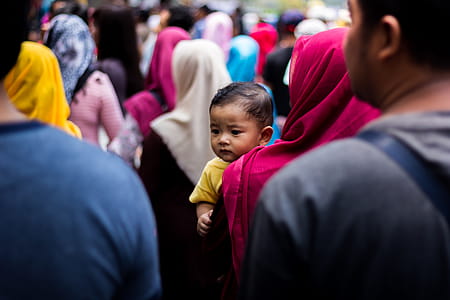 Baby Wearing Yellow T-shirt on Woman's Arm in Crowd thumbnail