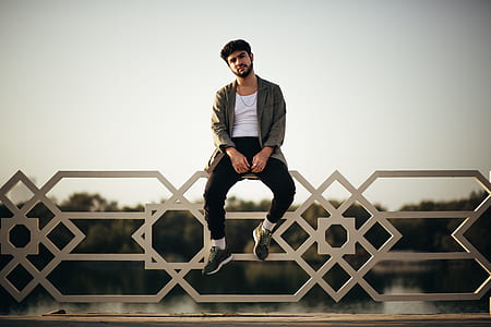 selective focus photography of man sitting on rails under gray skies thumbnail