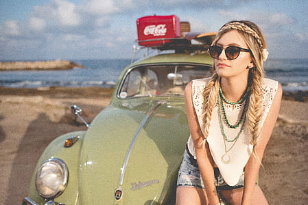 woman sitting in front of green Volkswagen Beetle on beach sand during daytime thumbnail