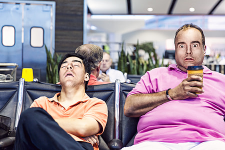 man making face sitting on gang chair beside man sleeping thumbnail