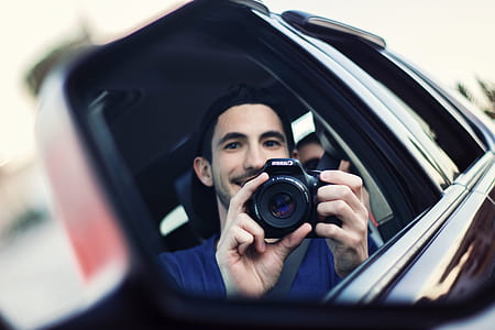 reflection of man holding black Canon DSLR camera thumbnail