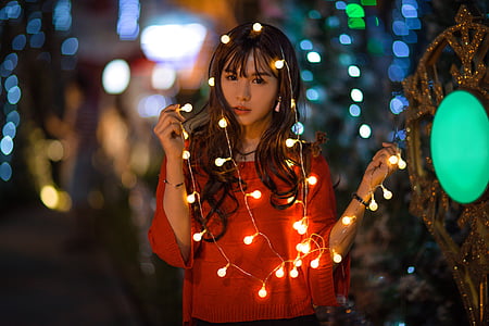 woman wearing red long-sleeved top holding string lights selective focus photography thumbnail