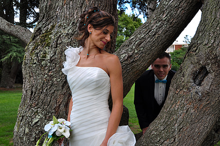 bride standing near groom hiding on tree during daytime thumbnail