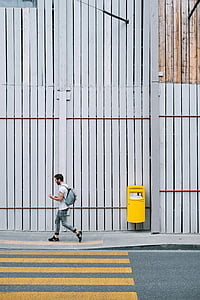 man walking while carrying backpack near mailbox and gray wall thumbnail