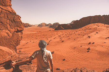 man standing near brown rocky mountain under white sky during daytime thumbnail