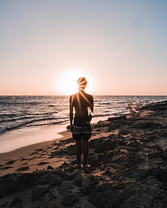 silhouette of man standing on rack looking at beach during golden hour thumbnail