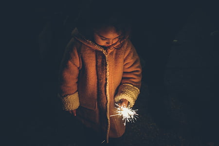 girl in brown coat holding lighted sparkler during nighttime thumbnail