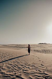 woman wearing black dress walking on sand background of open field thumbnail