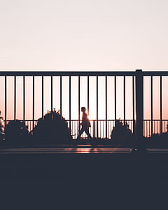 silhouette photo of person walking beside fence thumbnail