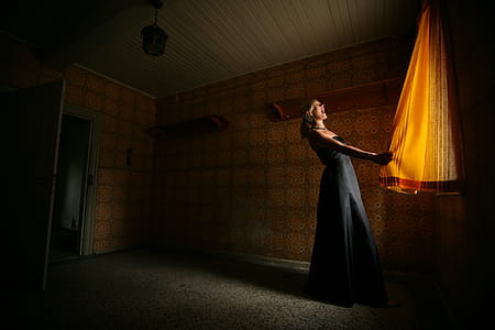 Standing Woman Wearing Black Dress Holding Curtain thumbnail