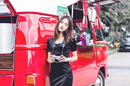 woman holding silver SLR camera leaning on red car thumbnail