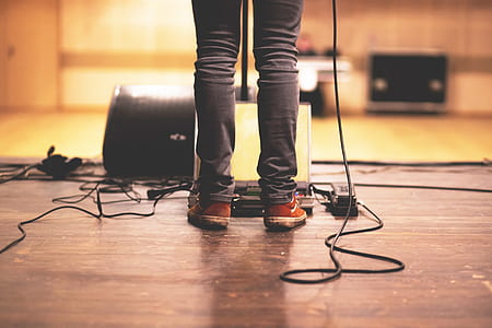 person wearing red sneakers and black denim jeans standing in front of opened laptop on wooden floor thumbnail