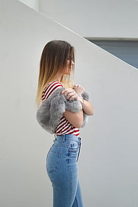 woman holding grey fur scarf standing beside white wall thumbnail