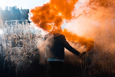 person holding orange smoke bomb standing on field thumbnail