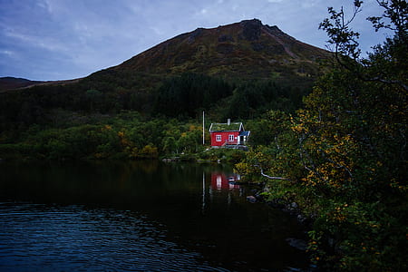 red house beside body of water near green mountain thumbnail