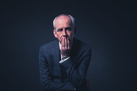 man wearing black suit covering his mouth with his fingers thumbnail