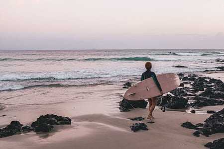 person holding brown surfboard on seashore thumbnail