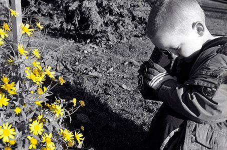 selective focus photo of child putting book on forehead while standing in front of yellow petaled flowers thumbnail